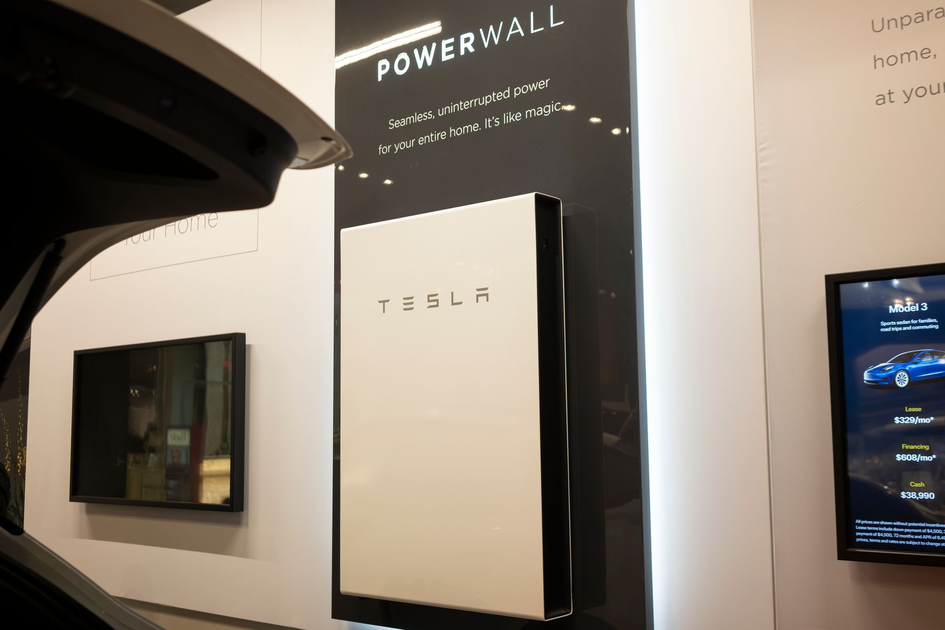 Tesla Powerwall battery display in a showroom with wall-mounted screens and signage