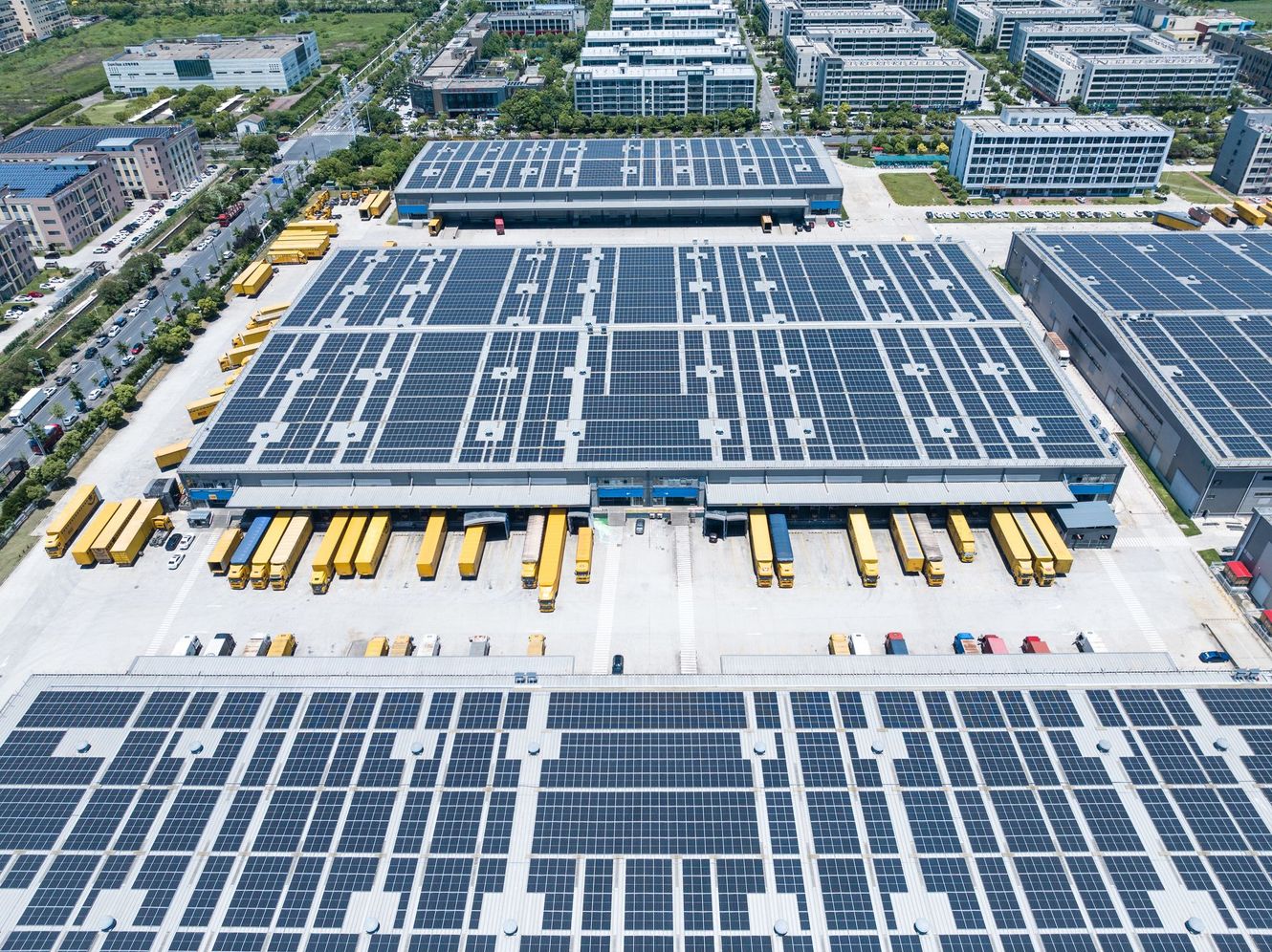Aerial view of a solar panel factory with rows of panels and yellow buses parked below