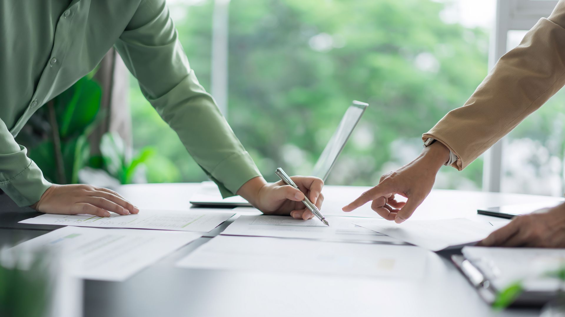 People signing documents at a bright office table with laptops and papers