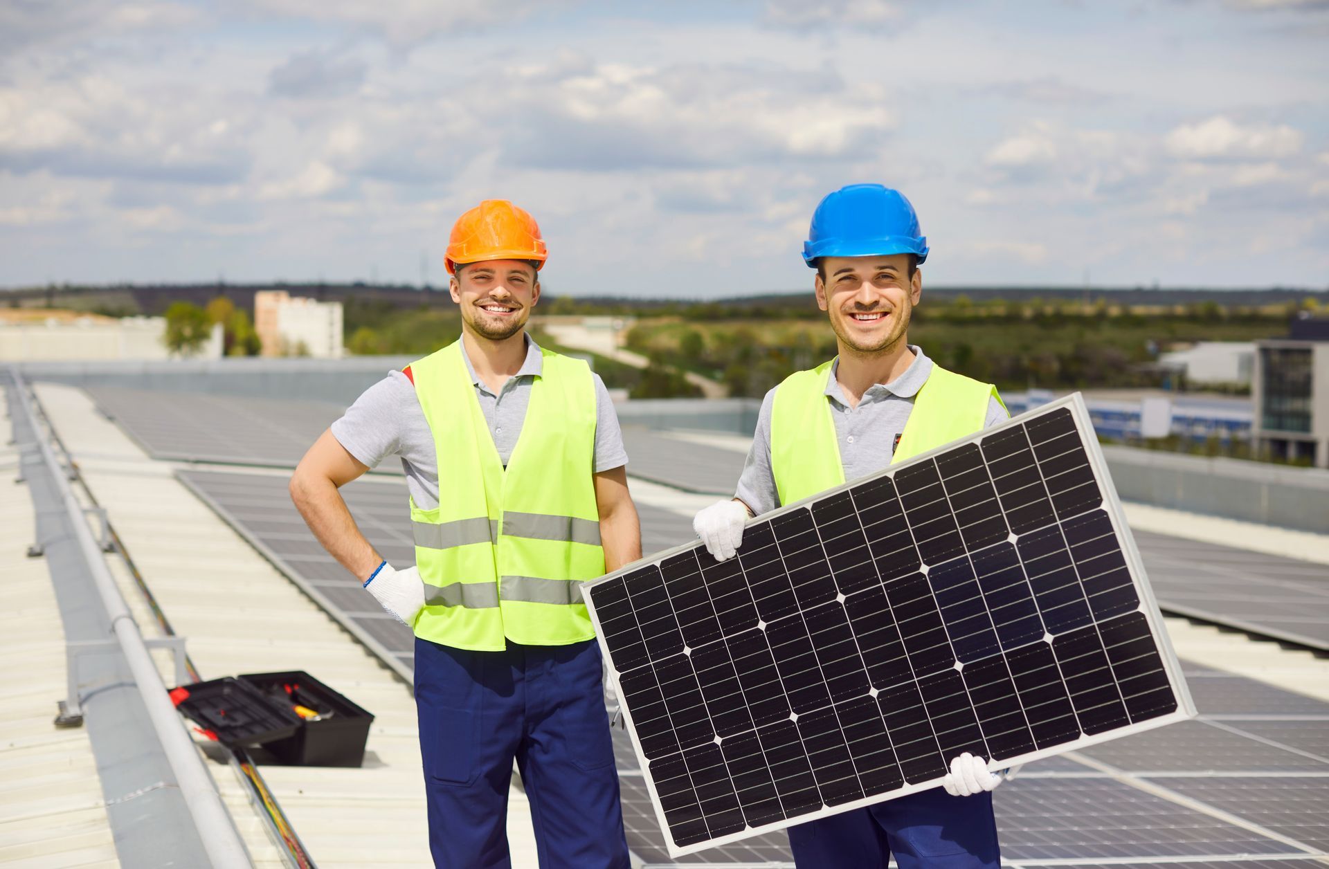 Two workers on a rooftop holding a solar panel, with rows of panels in the background.