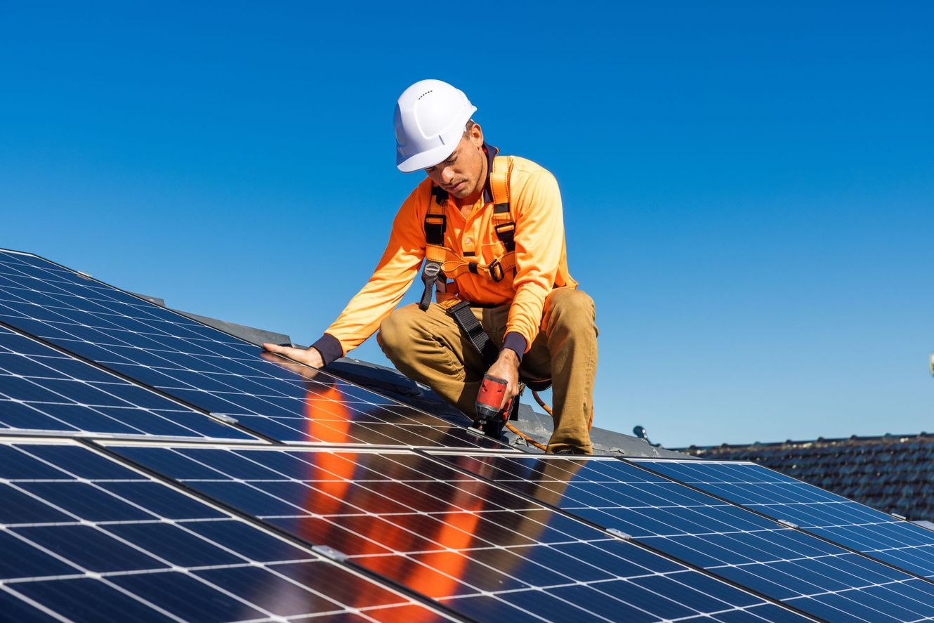 Worker in hard hat inspecting solar panels under a clear blue sky