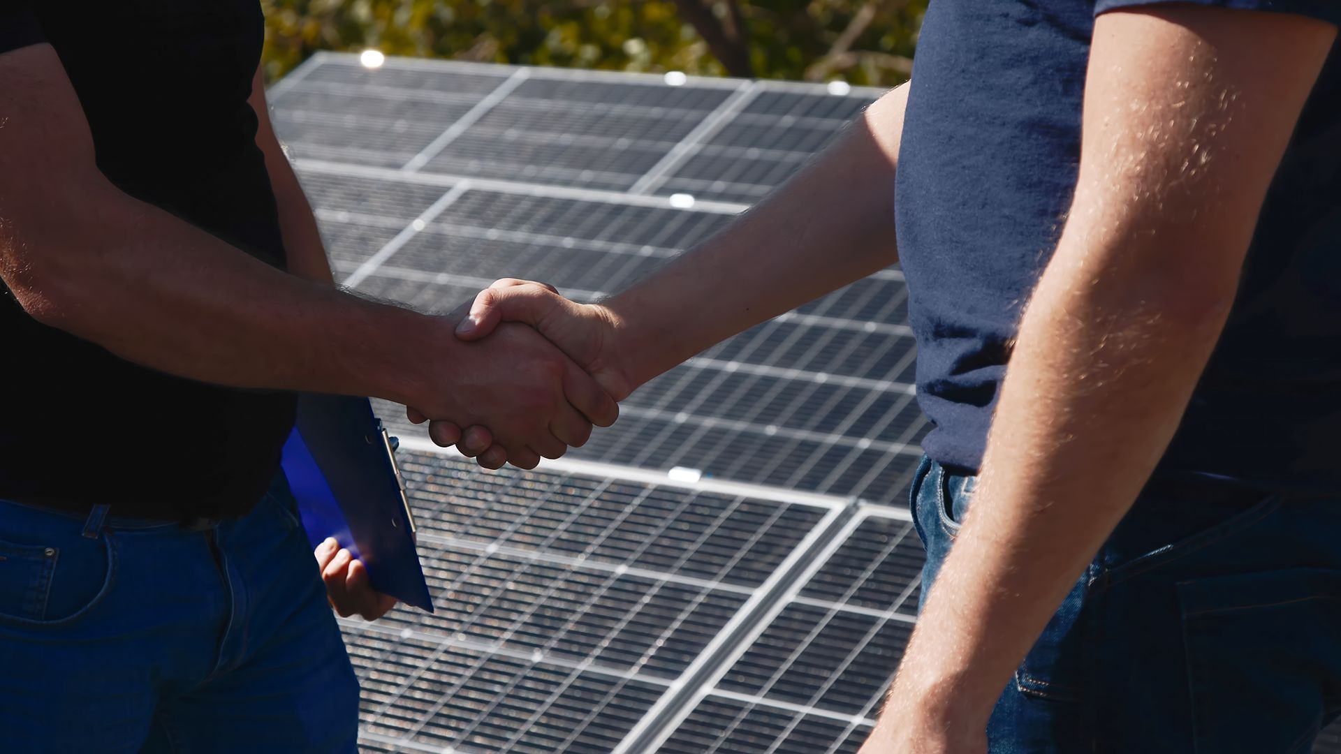 Two people shaking hands beside solar panels outdoors