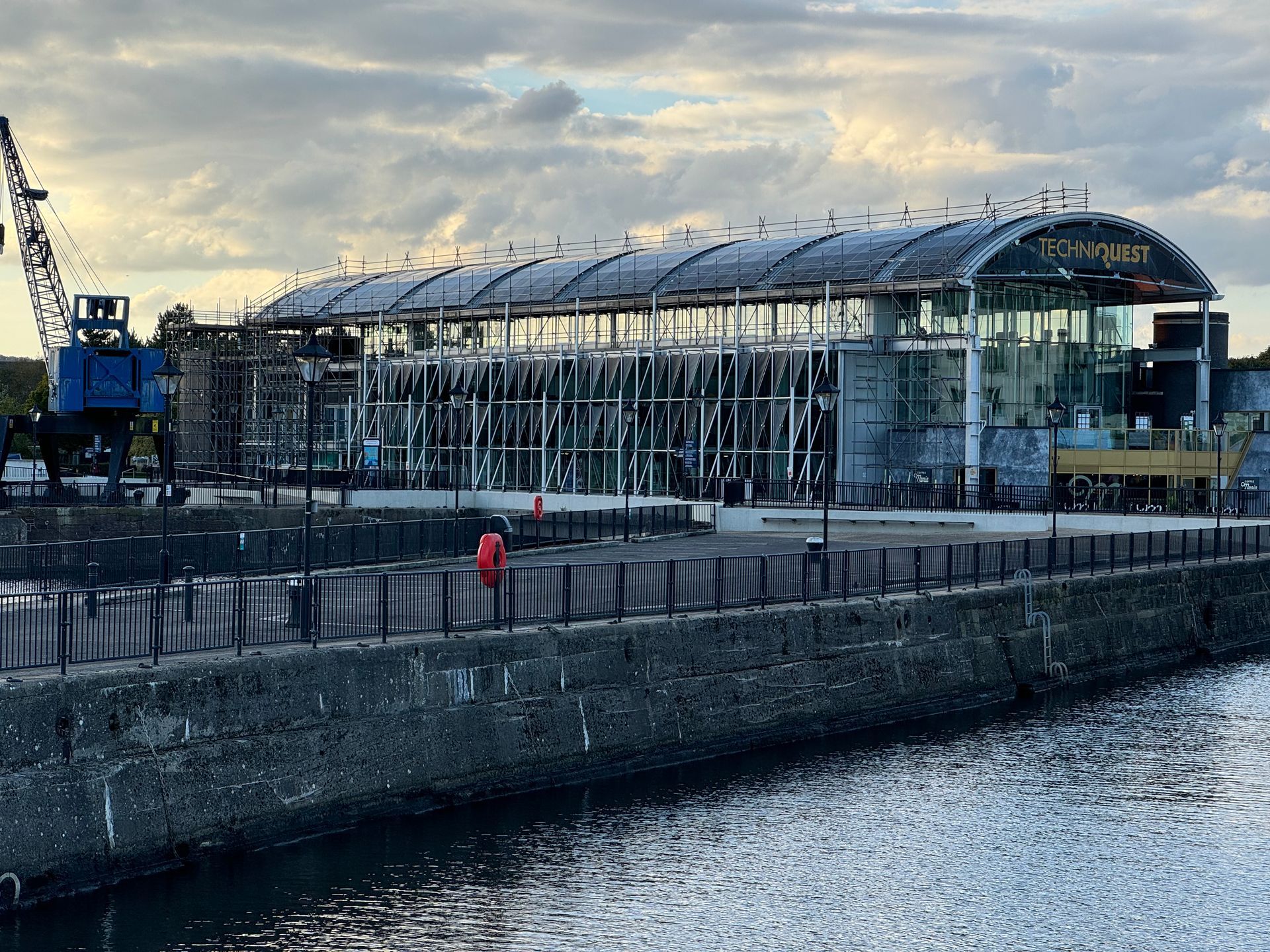 Modern glass train station by a waterfront at dusk, with a person in red on the promenade