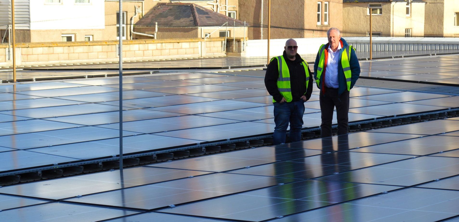 Two workers in high-visibility vests standing on a reflective rooftop under construction