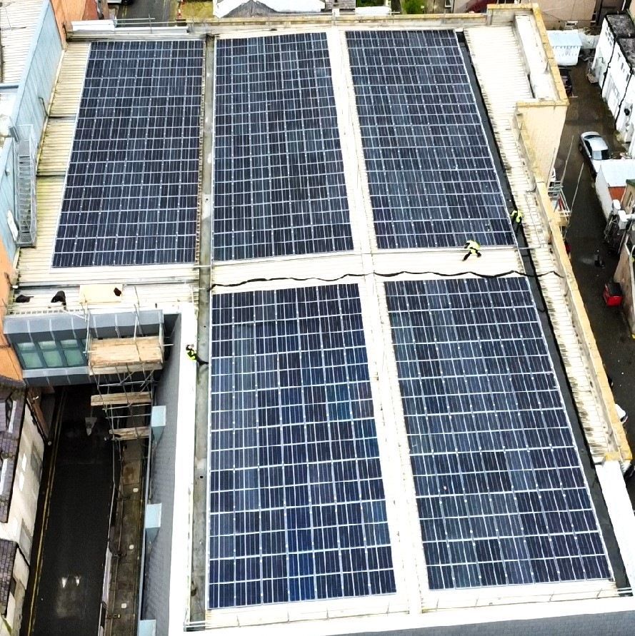 Aerial view of a rooftop covered with large solar panels in rectangular sections.