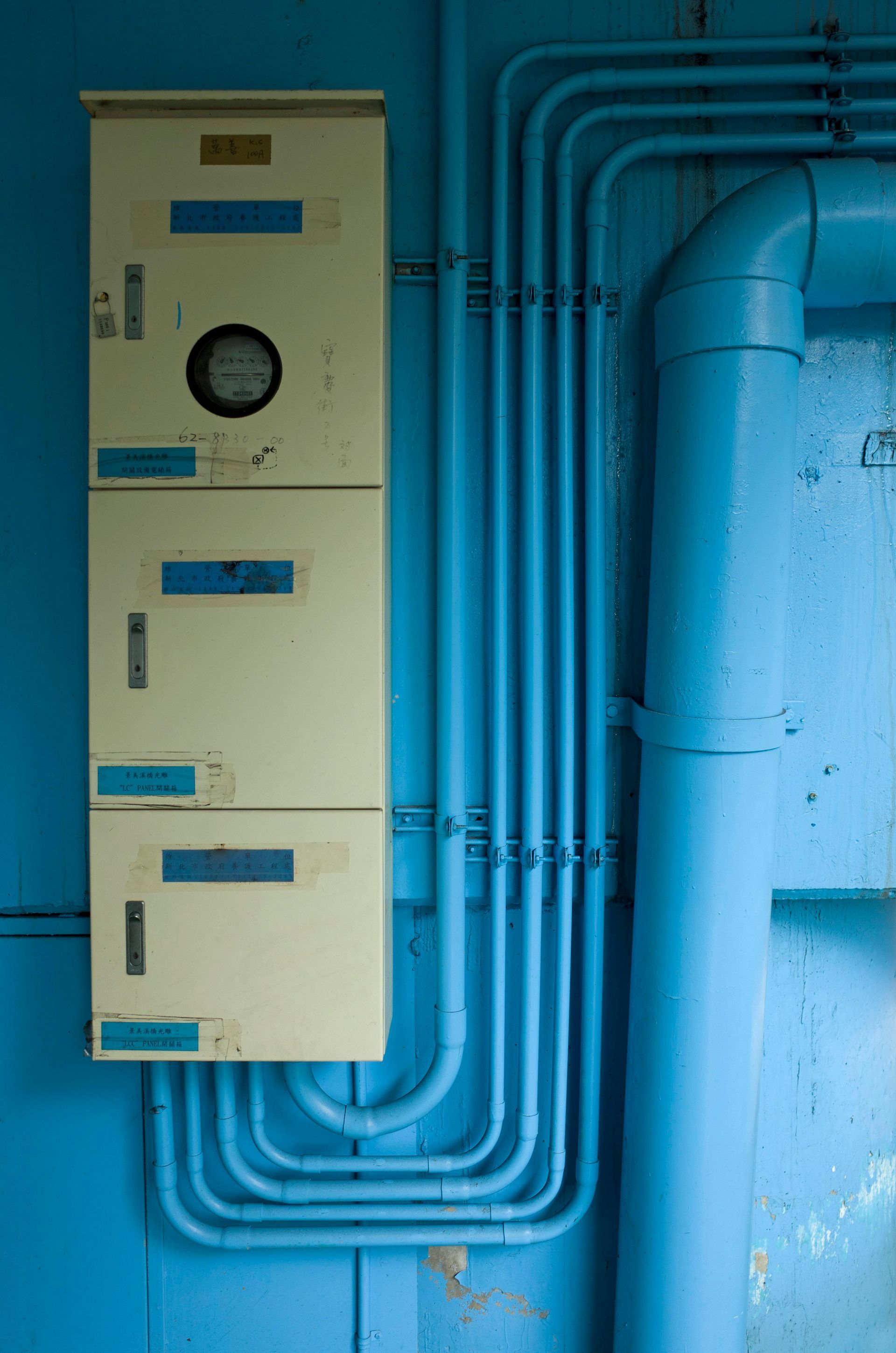 Blue electrical panel with exposed conduit pipes on a wall