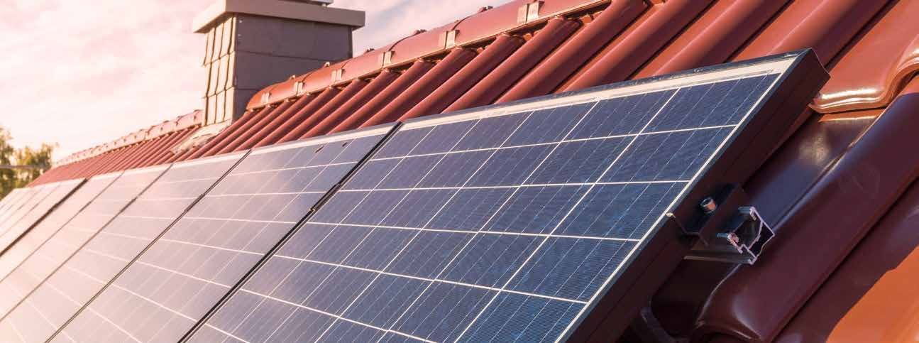 Solar panels mounted on a sloped red roof in warm sunlight.