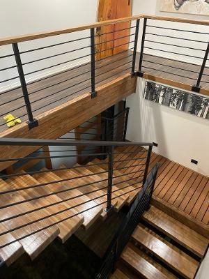 Wooden staircase with black metal railings, leading to a wooden platform and upper level with similar railings.