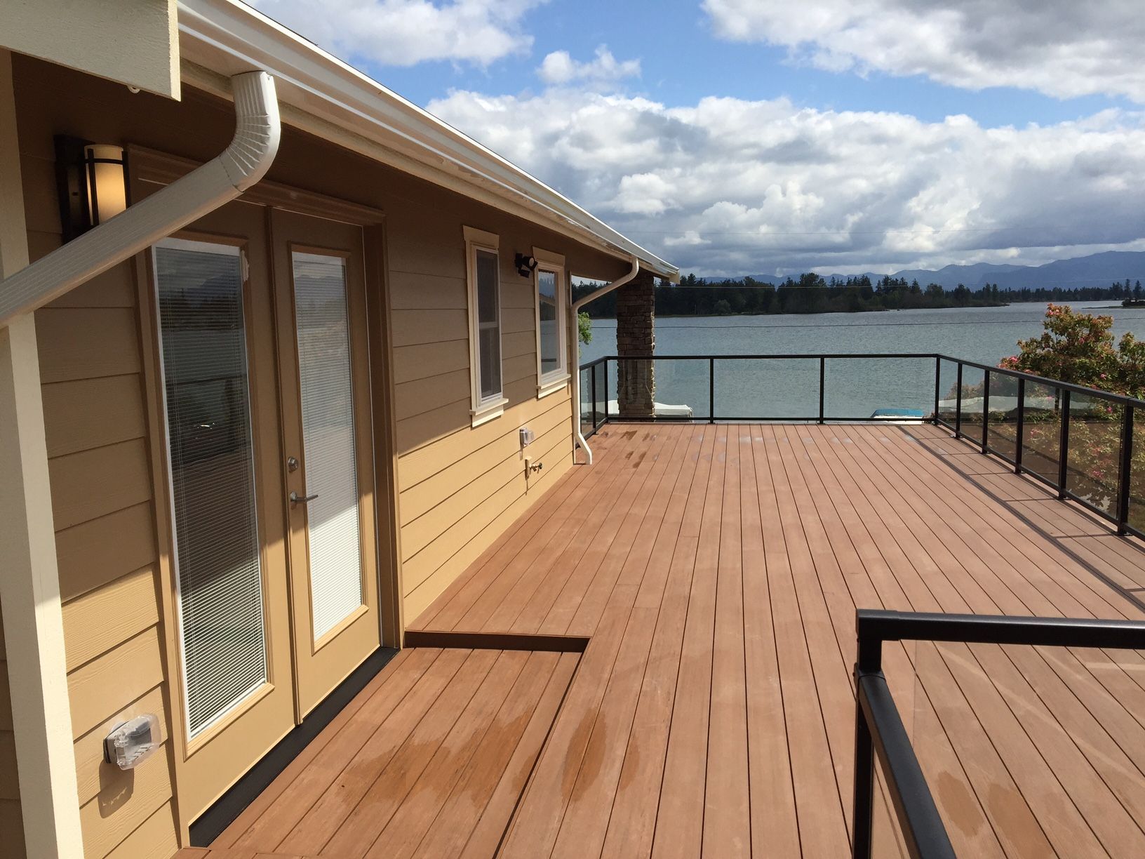 House with a wooden deck overlooking a lake, cloudy sky.