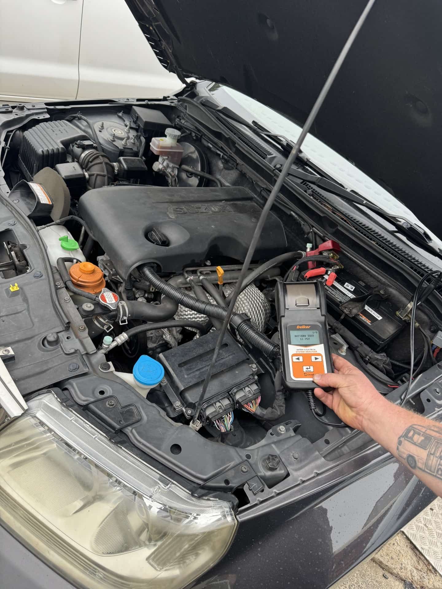 A person is holding a battery tester under the hood of a car. — Noosa Batteries in Noosaville, QLD