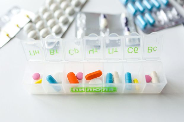 Weekly pill organizer with assorted colorful medication capsules and tablets on a white surface