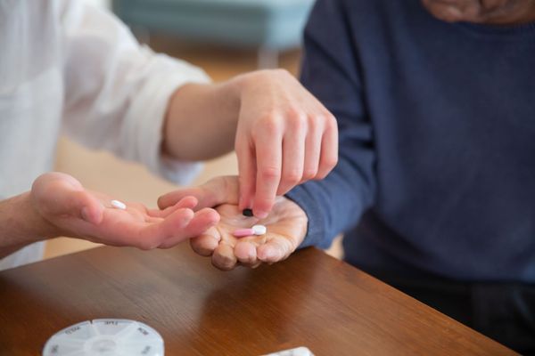 Hands passing small pills over a wooden table, with a pill bottle in the foreground
