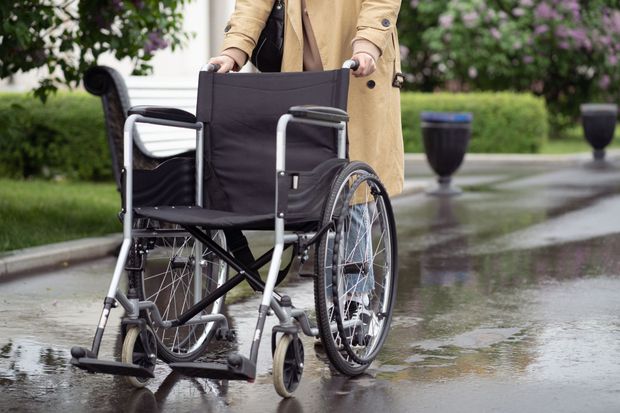 Person pushing a black wheelchair on a wet path in a park