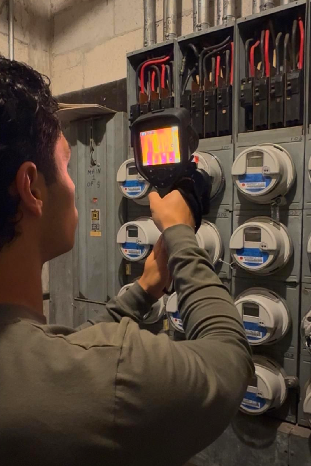 Technician using an infrared camera to inspect electrical meters in a utility panel