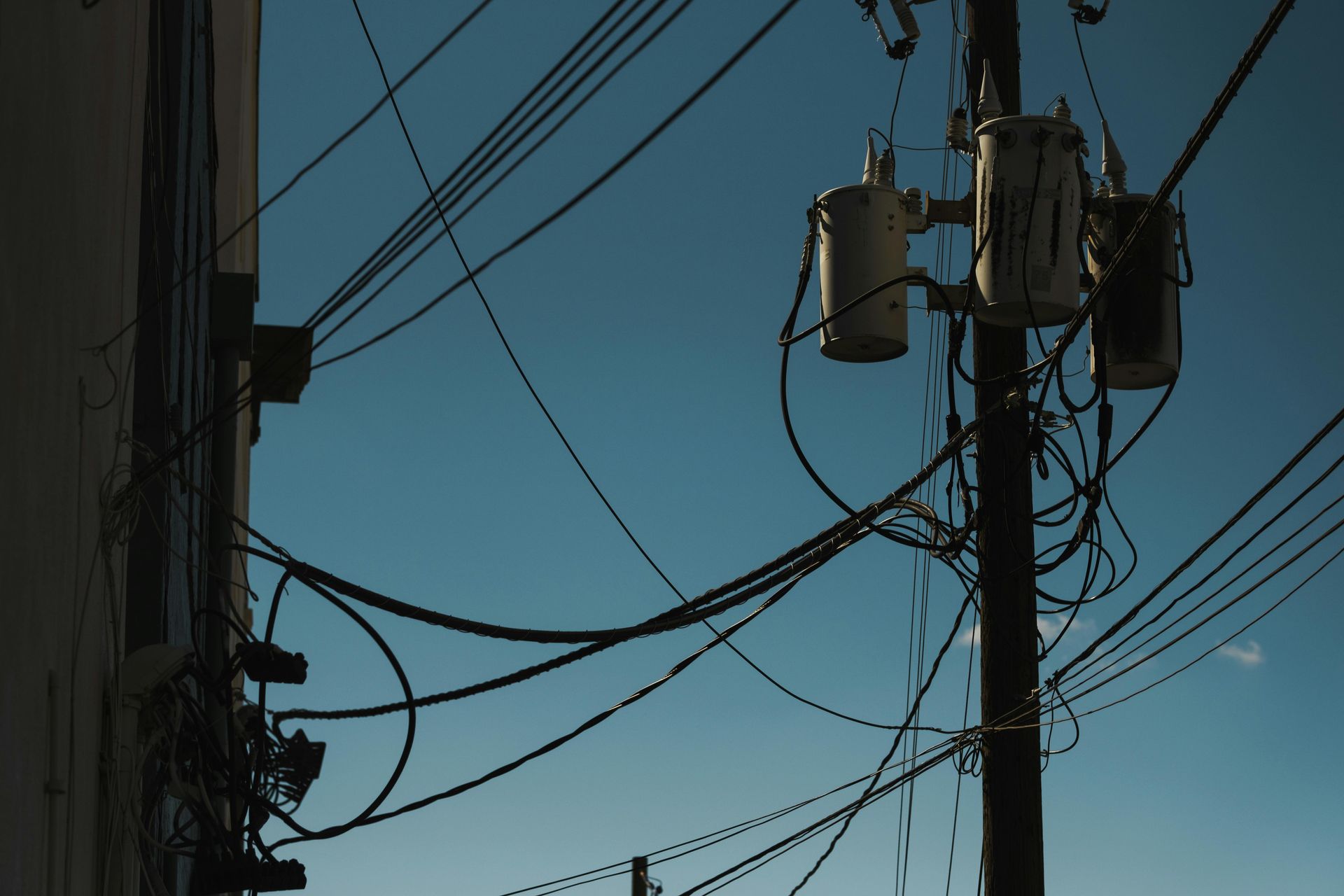 Utility poles and tangled power lines silhouetted against a clear blue sky
