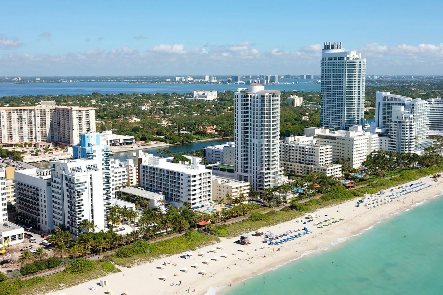 Aerial view of beachfront high-rise hotels, white sand, and turquoise ocean under a clear sky