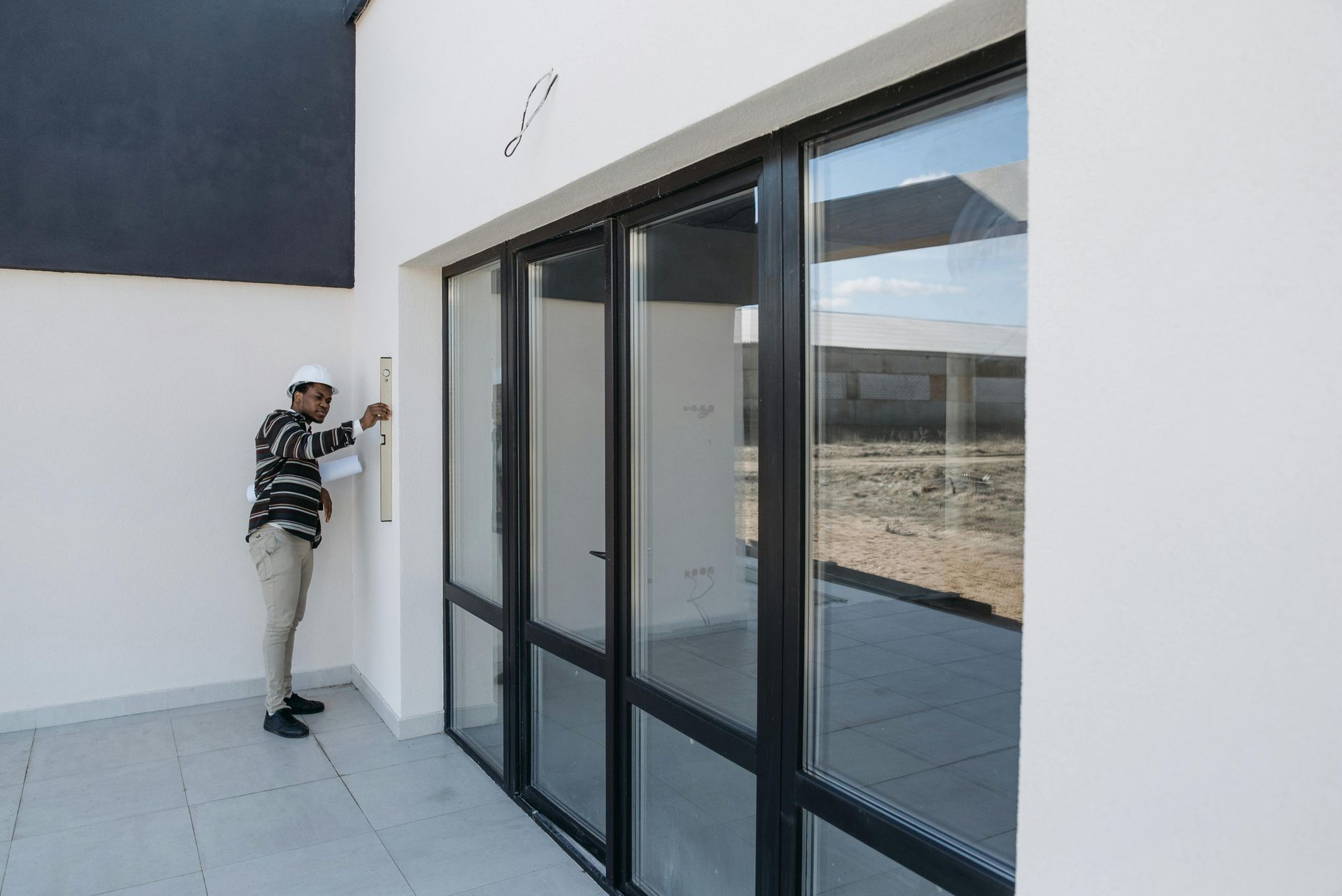 Person inspecting a wall beside large glass sliding doors on a modern patio.