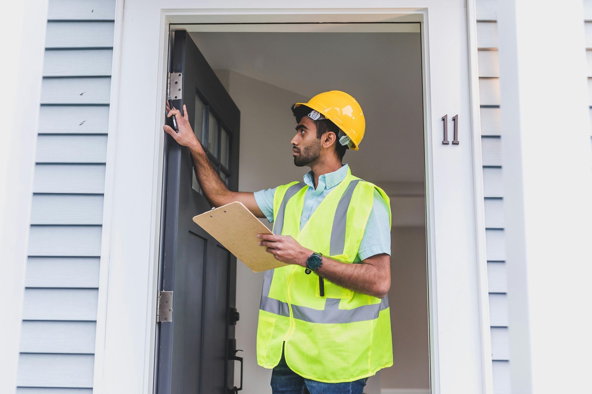 Construction inspector in yellow hard hat and vest checking a front door with clipboard
