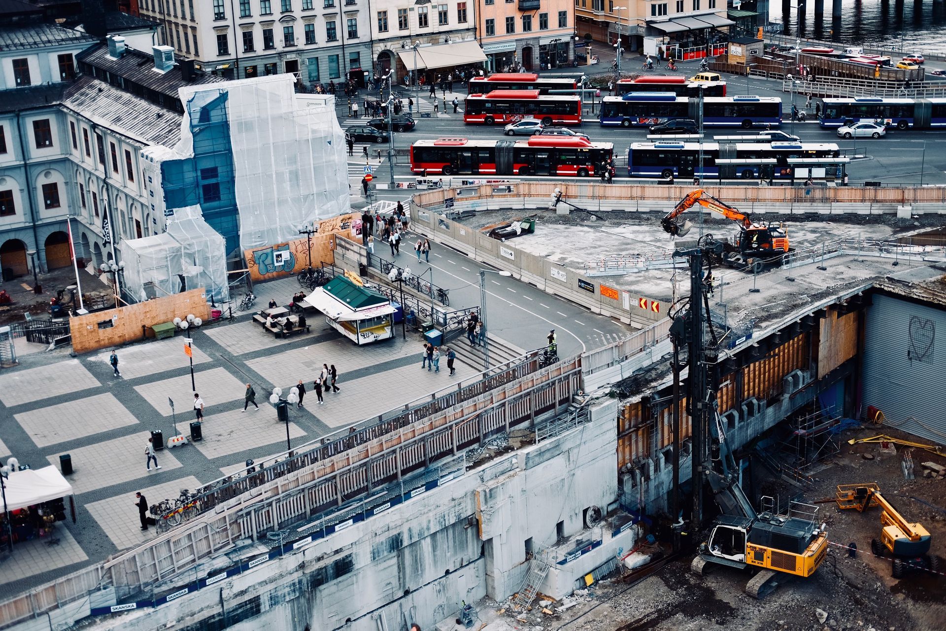 Construction site with excavators and workers beside a partially demolished concrete building in a city.