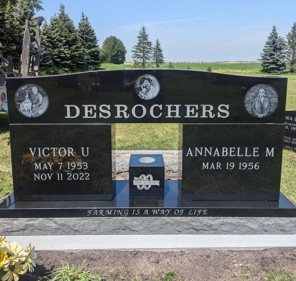 Black granite gravestone for the Desrochers family in a cemetery, with trees and blue sky behind it