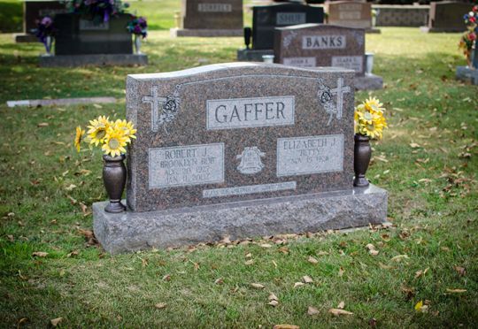 Gravestone in a cemetery with sunflowers in vases and a smaller headstone behind it.