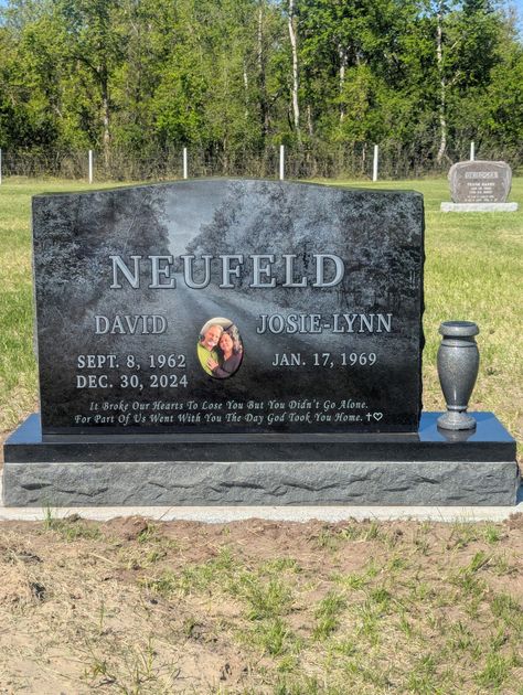 Black granite gravestone with flowers and a vase in a wooded cemetery.