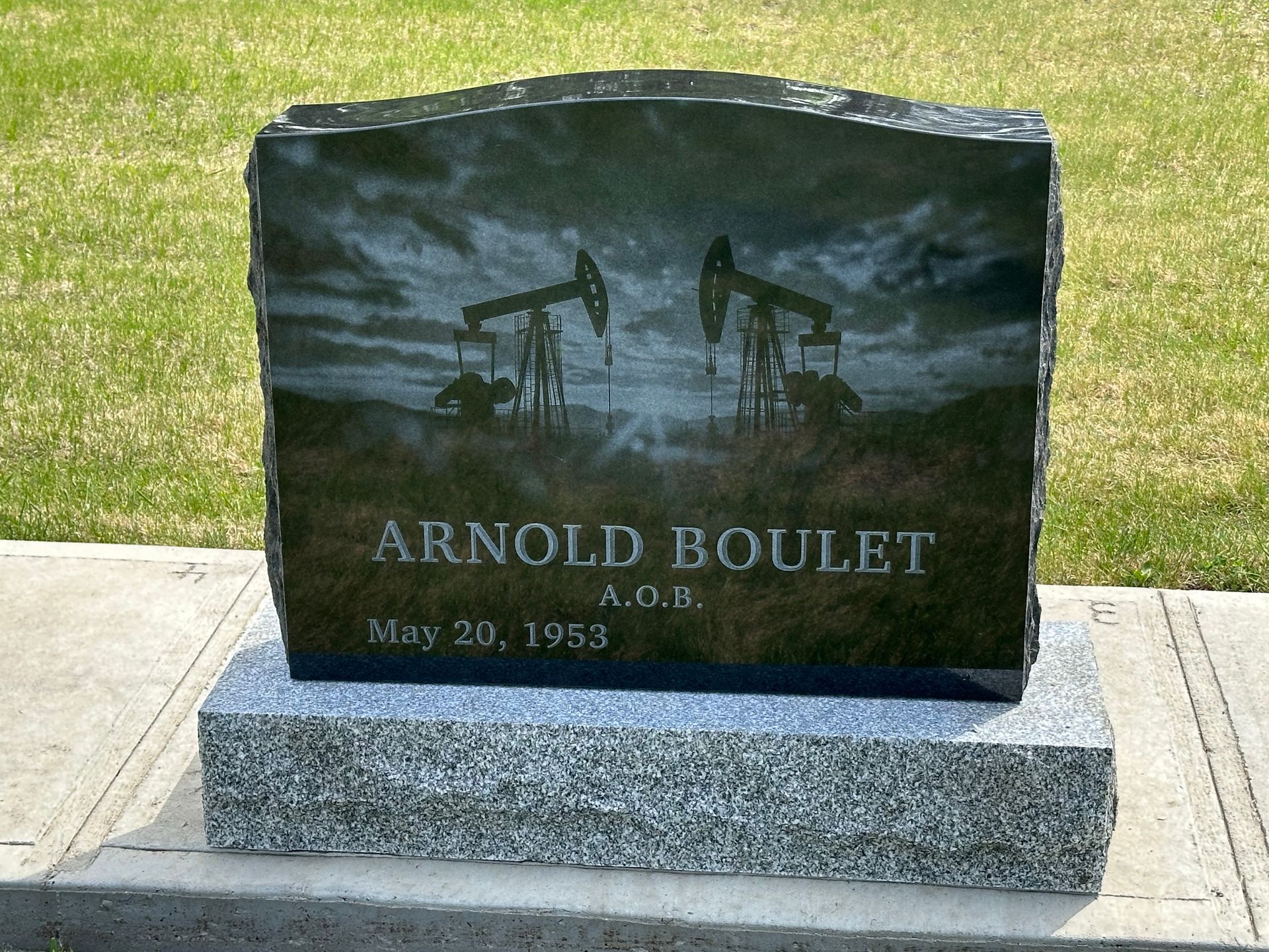 Gravestone for Arnold Boulet with oil derrick engraving in a grassy cemetery