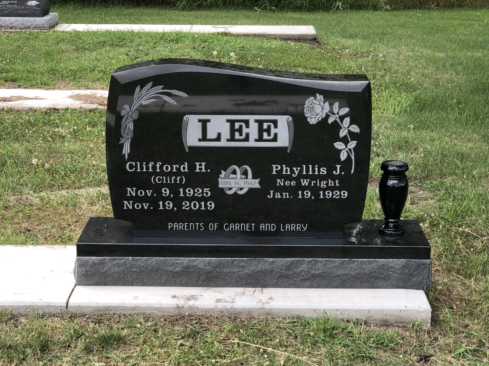 Black gravestone with “LEE,” flowers, and names/dates in a cemetery.