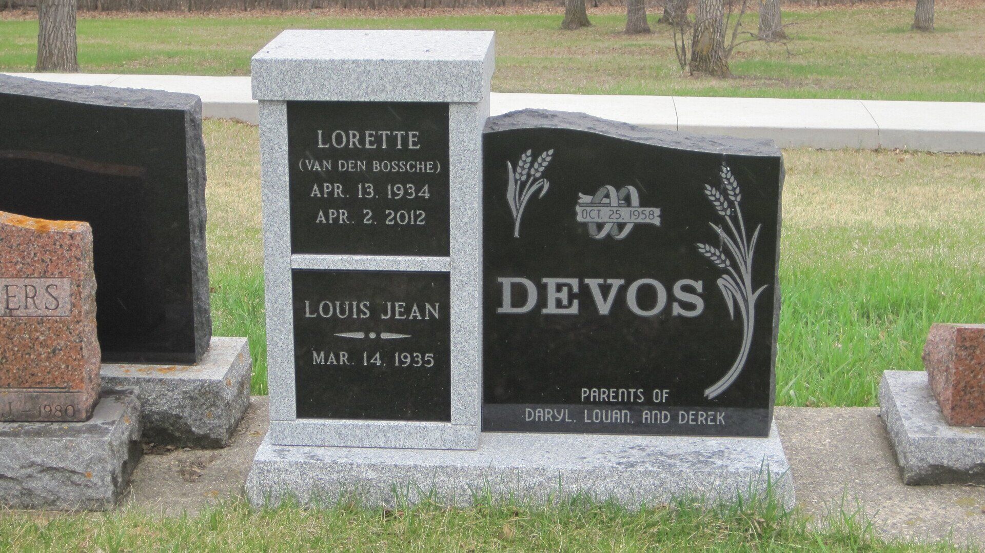 Two black granite gravestones in a cemetery, one engraved “DEVOS” with a flower design