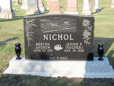 Black granite grave marker on a white base in a cemetery, engraved with the name Nichol and flowers on both sides