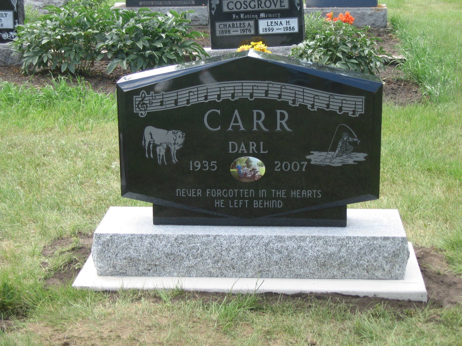 Black gravestone memorial for Darl and Carrie in a grassy cemetery, with flowers behind it