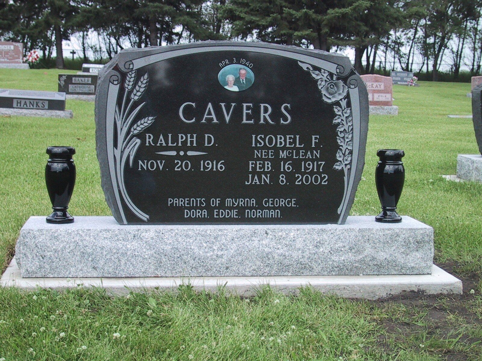 Black gravestone with carved names Ralph D. Cavers and Isobel F. in a grassy cemetery