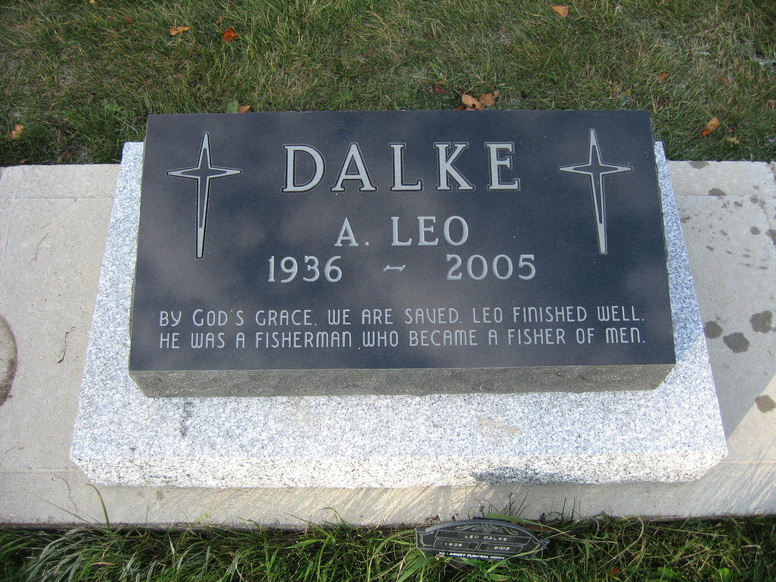Black granite gravestone engraved “DALKE A. LEO 1936–2005” on a concrete base in grass.