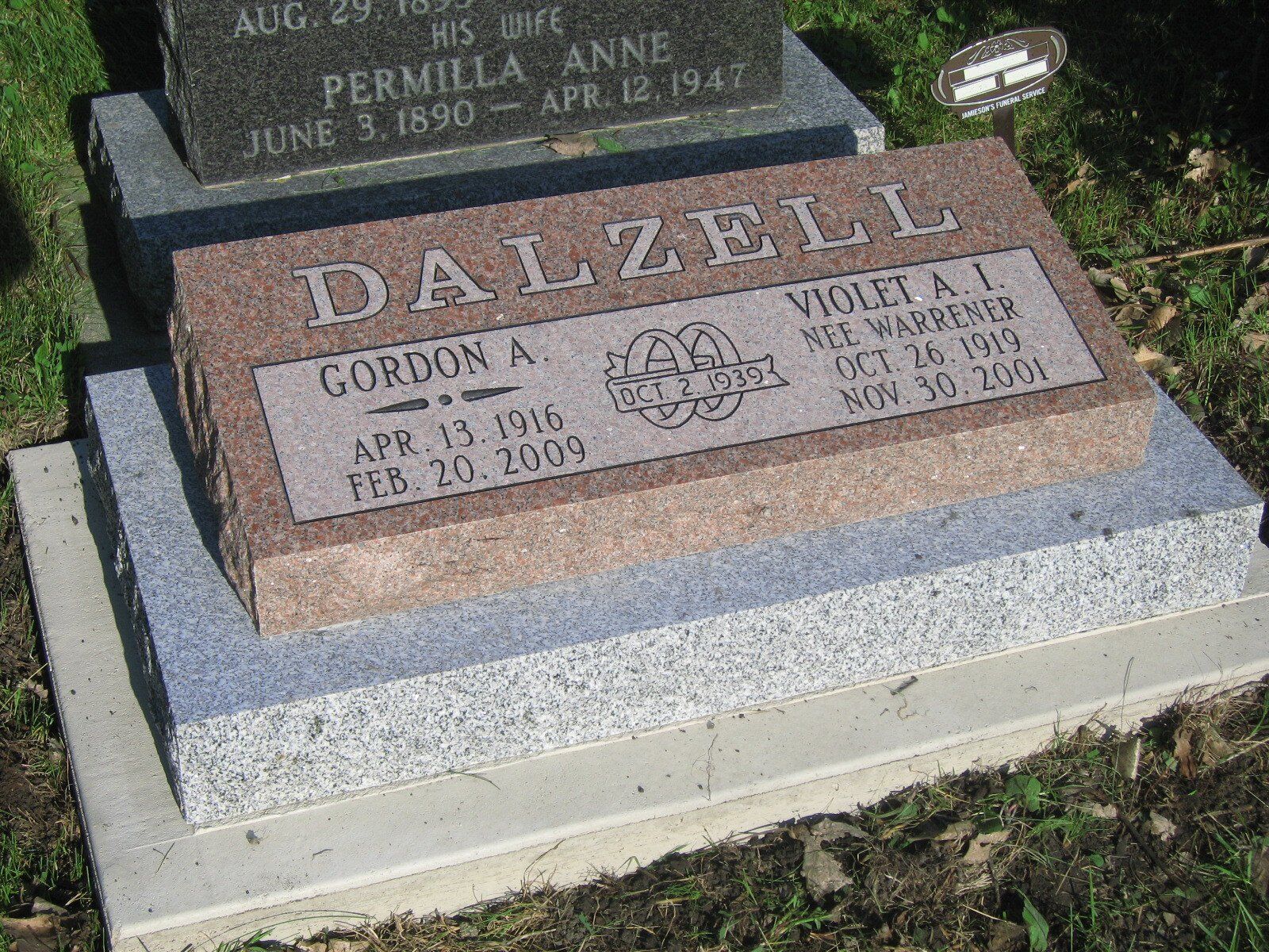 Two brown gravestones on a concrete base in a grassy cemetery, with the name DALZELL engraved on the front stone