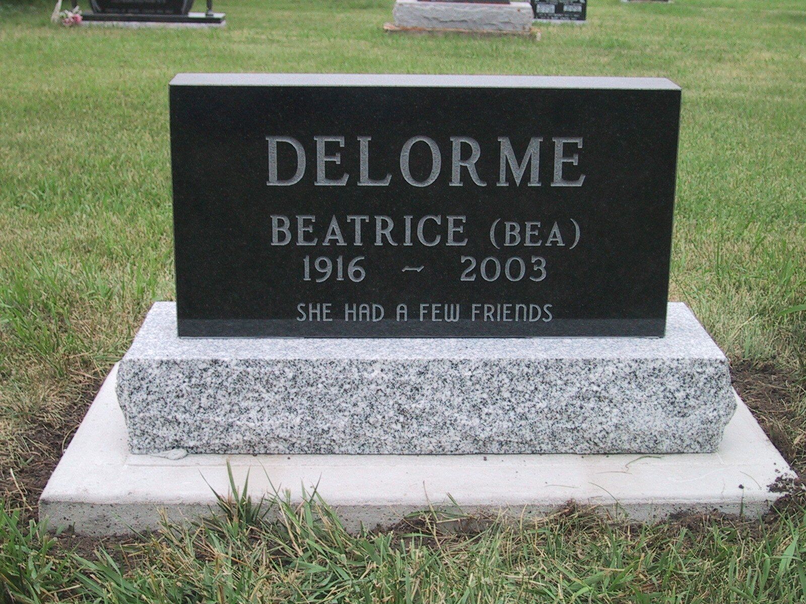 Gravestone for Beatrice Delorme in a grassy cemetery, black plaque on a white base.