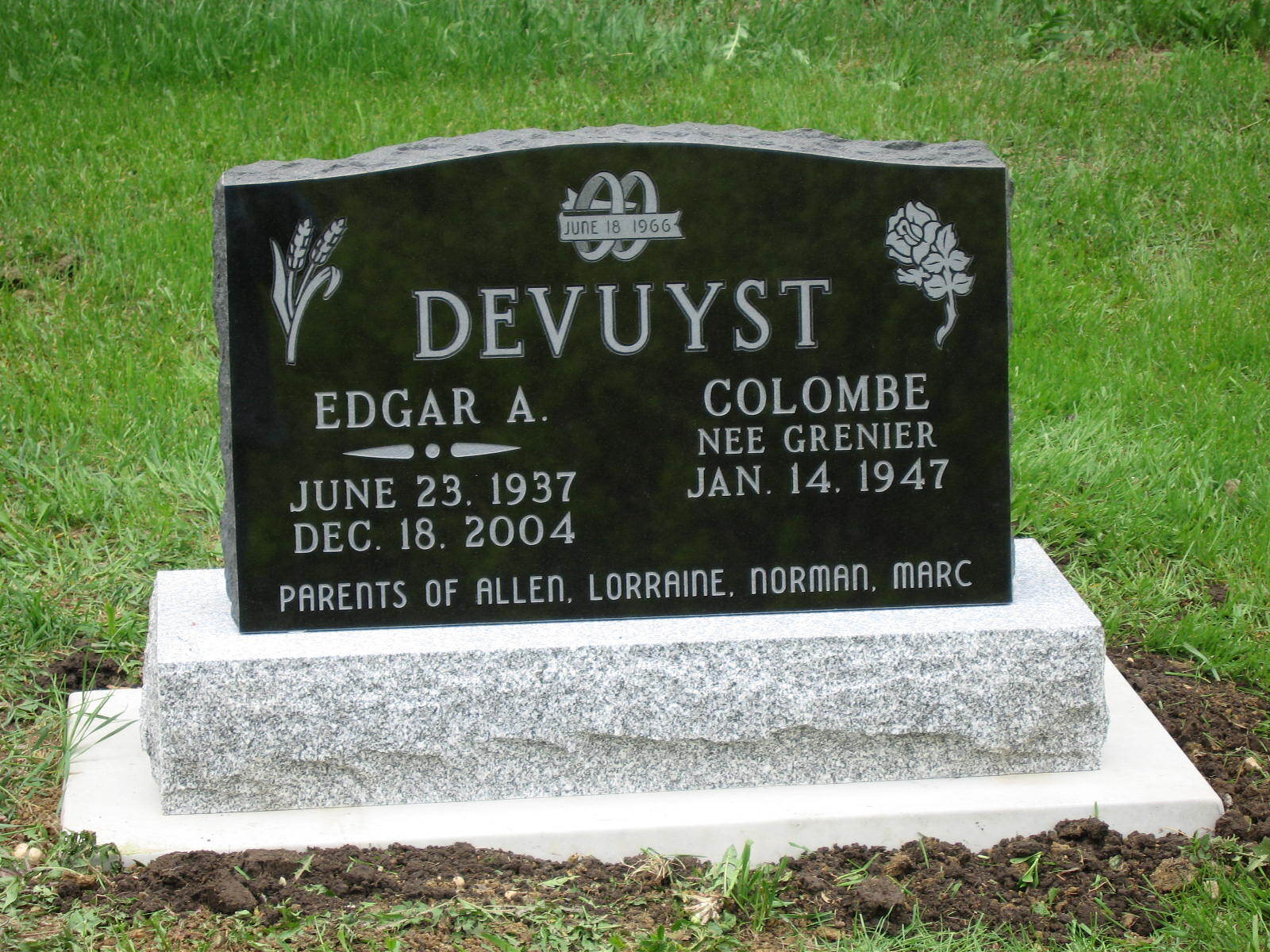 Black granite gravestone with the name Devuyst in a grassy cemetery.