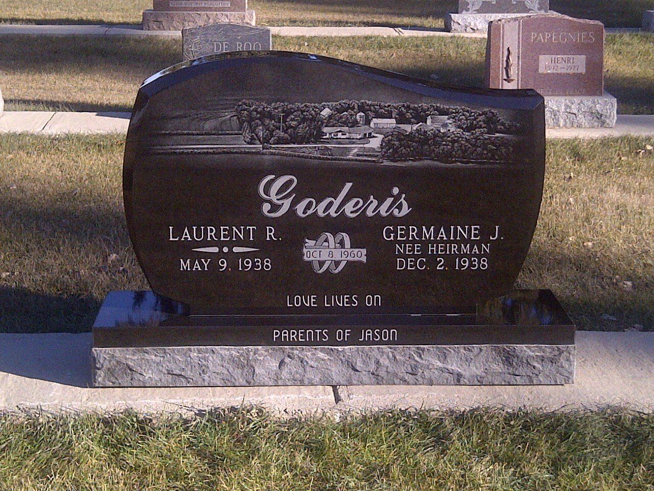 Black gravestone marker engraved “Soderis” in a cemetery, with flower beds around it.