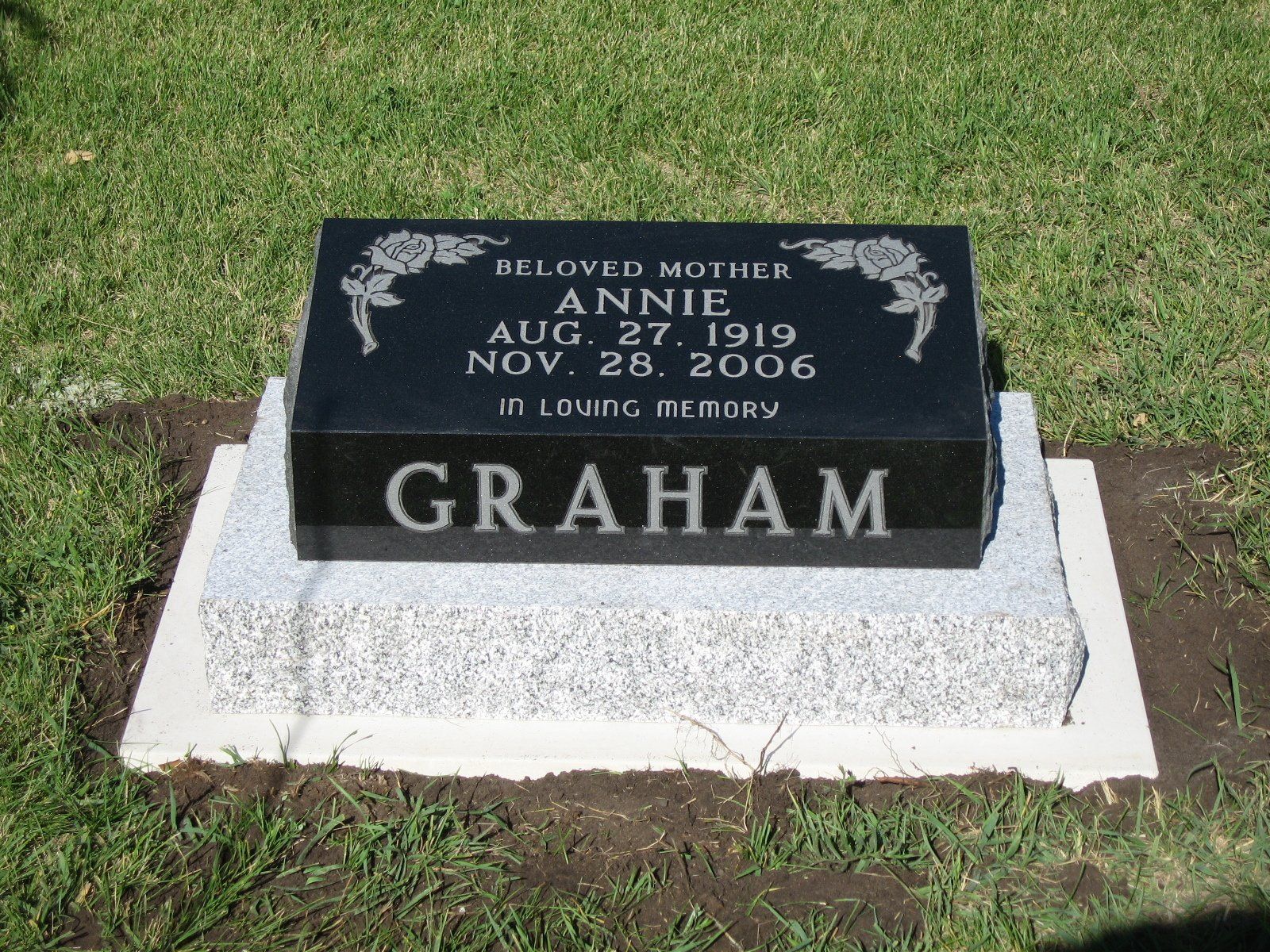 Black granite memorial marker for D. Lovelle Mitchell Graham with dates, on a white base in grass.