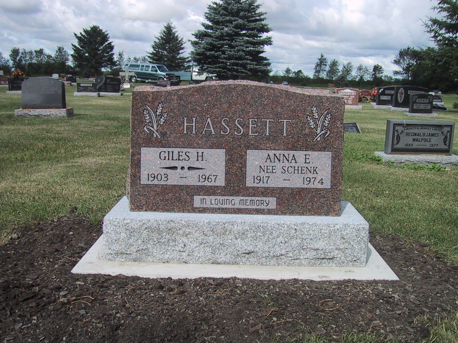 Brown granite memorial headstone in a cemetery, with engraved names and dates on a gray base.