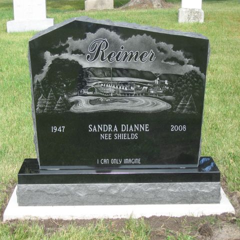 Black granite memorial headstone with “Reimer” and engraved landscape, in a cemetery
