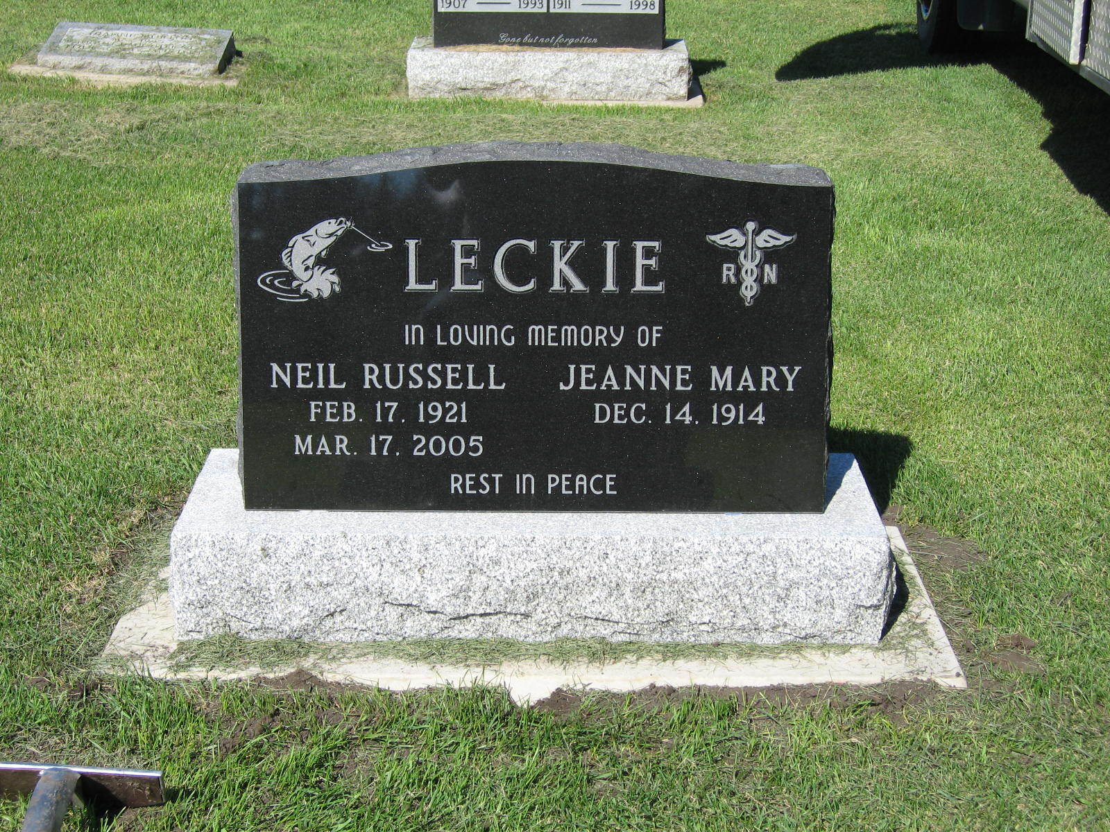 Black memorial headstone with white lettering in a grassy cemetery