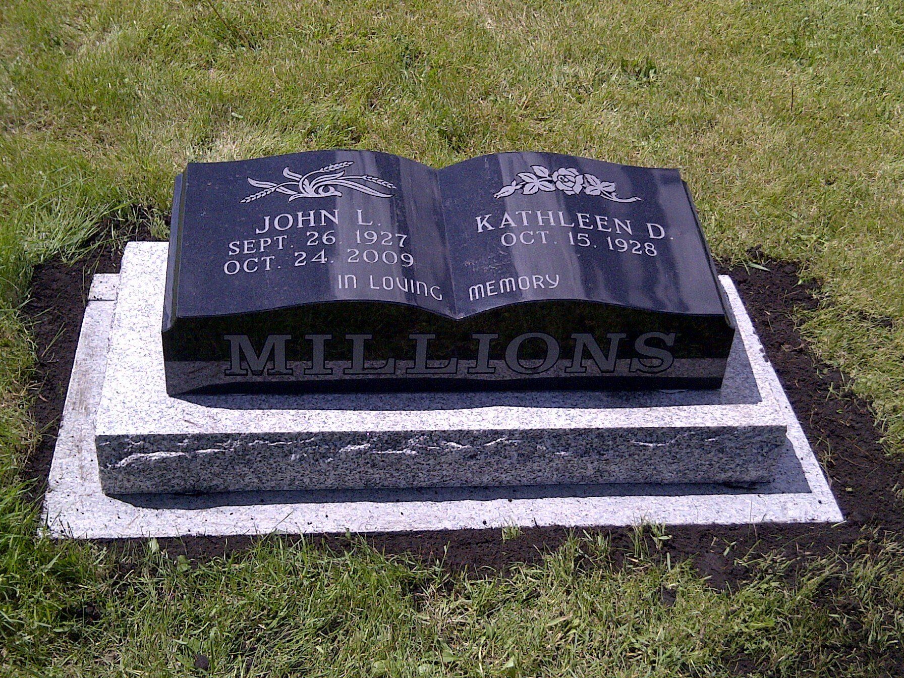Black granite grave marker on a white base in a grassy cemetery.