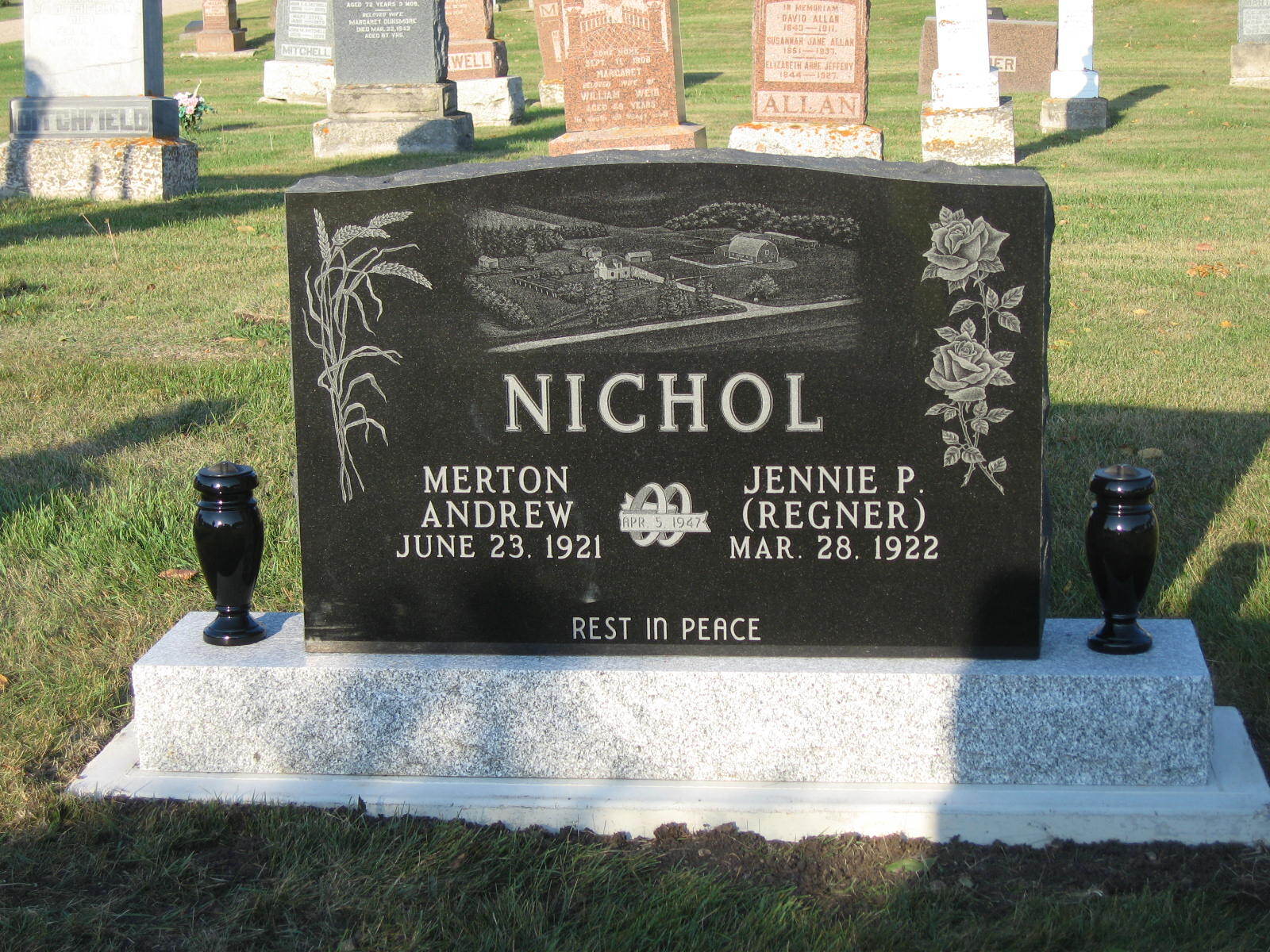 Nichol gravestone in a cemetery, black marker on gray base with floral carvings and two black vases.