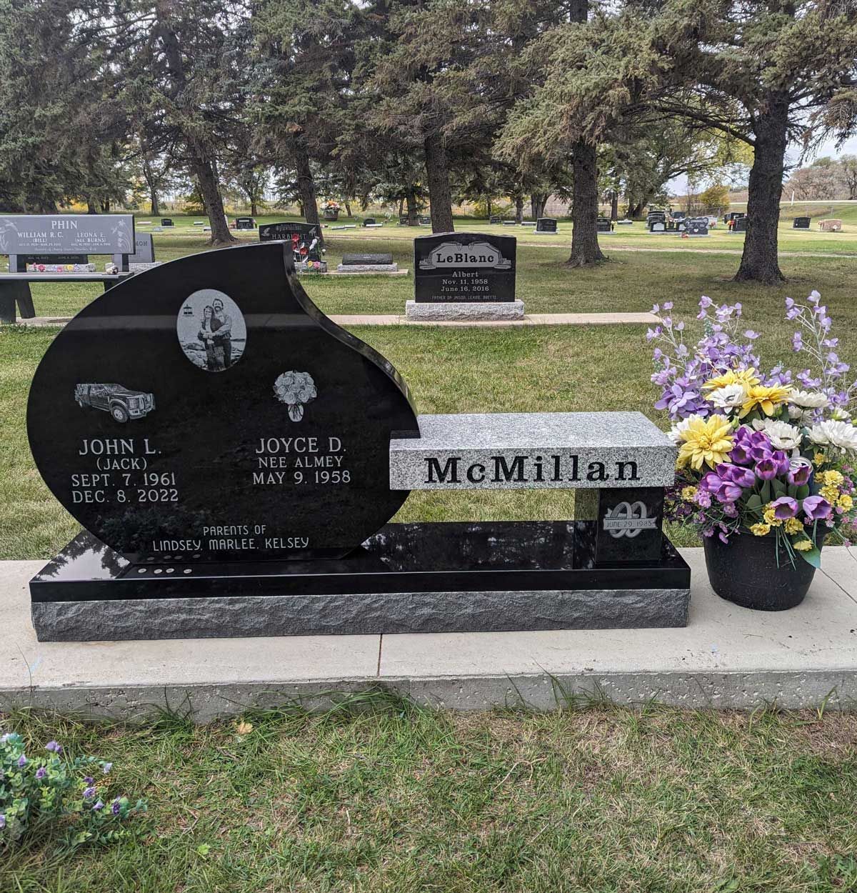 McMillan grave marker with black and gray headstone and purple flowers in a cemetery