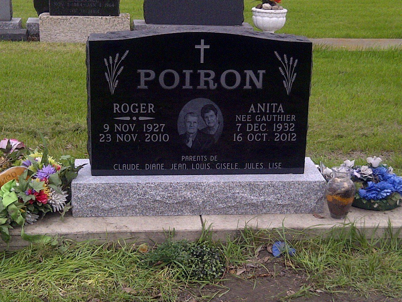Black gravestone with flowers, engraved POIRON, in a cemetery lawn.