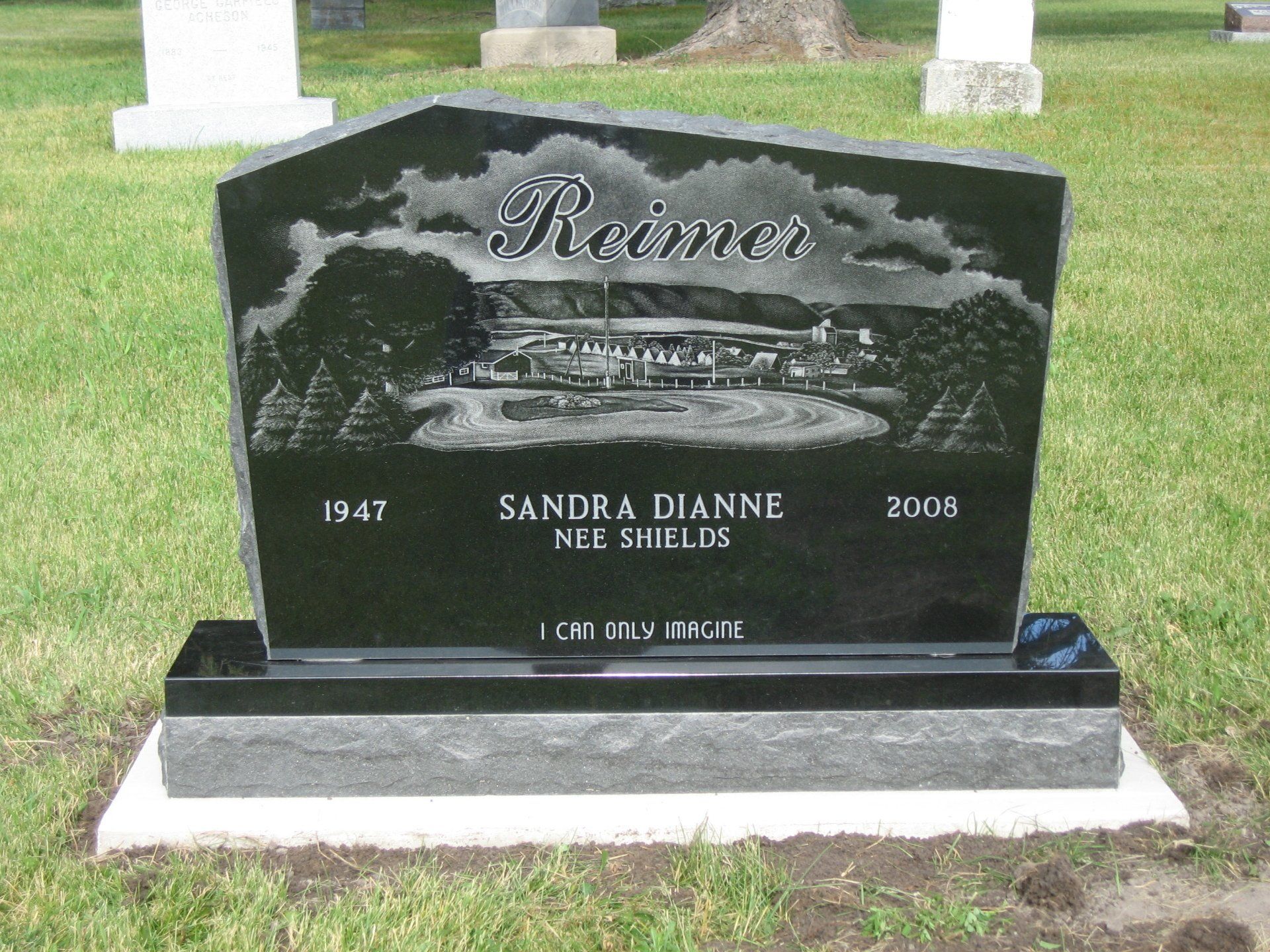 Black granite gravestone with engraved car and surname “Reince” in a cemetery