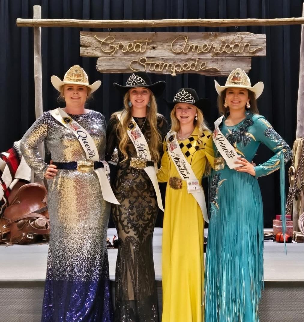 Four women are posing for a picture in front of a sign that says open american stampede