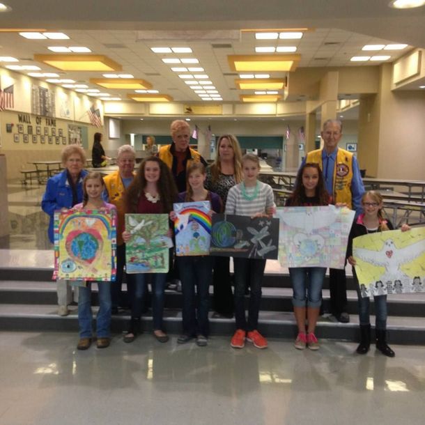 A group of people are posing for a picture while holding paintings