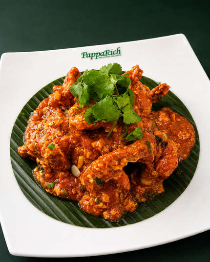 Spicy orange-red curry topped with cilantro, served on a white square plate with a dark green leaf lining.