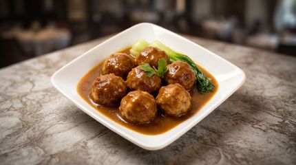 Brown meatballs in glossy sauce on a white square plate on a marble table.